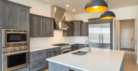 A modern kitchen with white quartz worktops. There are two grey and yellow pendant lights hanging over a kitchen island and wall units are grey.