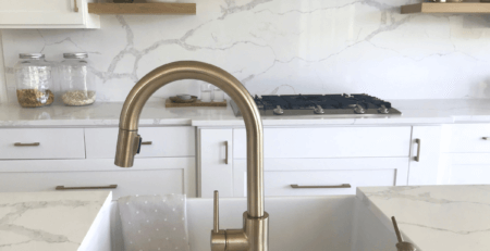 close up of a ceramic kitchen sink with marble surround. The large tap of brushed chrome is set into the marble.