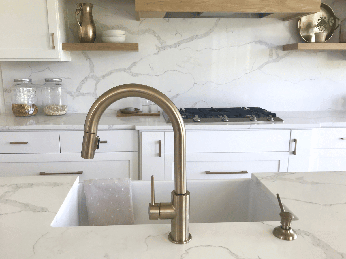 close up of a ceramic kitchen sink with marble surround. The large tap of brushed chrome is set into the marble.