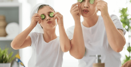 A mother and daughter in white t-shirts and their hair in towels playfully put cucumber slices in front of their eyes in a new family bathroom.