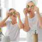 A mother and daughter in white t-shirts and their hair in towels playfully put cucumber slices in front of their eyes in a new family bathroom.