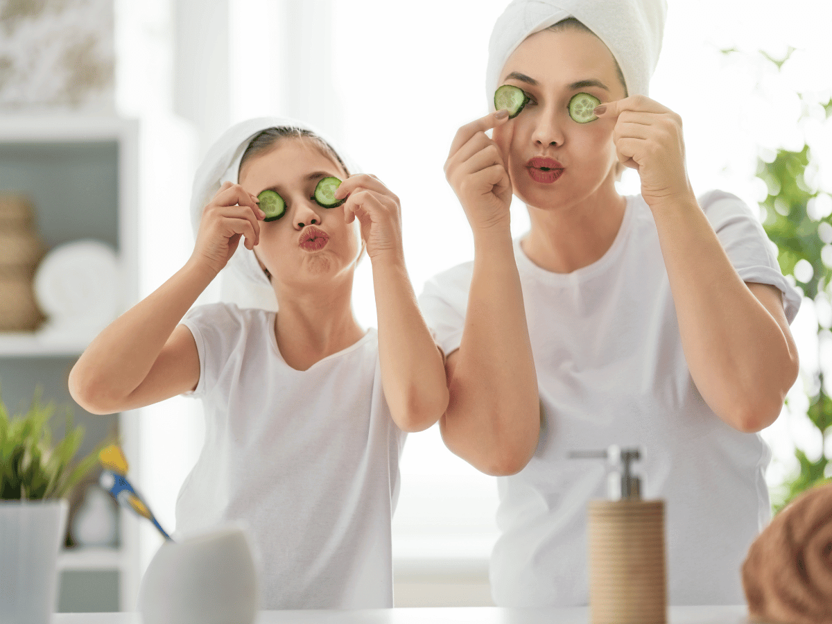 A mother and daughter in white t-shirts and their hair in towels playfully put cucumber slices in front of their eyes in a new family bathroom.